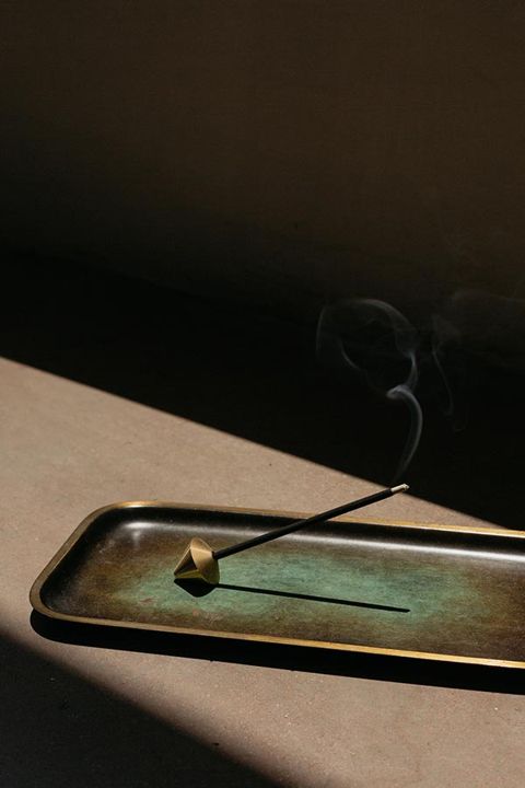 An elemense incense stick burning on a brass tray, smoke rising in warm light